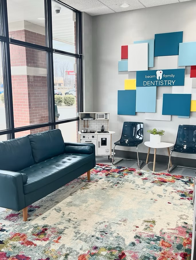 The bright, family-friendly waiting room at Beam Family Dentistry in Louisville, KY, featuring a teal sofa, colorful accent wall, and children's play area.